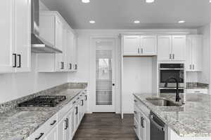 Kitchen with appliances with stainless steel finishes, sink, white cabinets, light stone counters, and wall chimney range hood