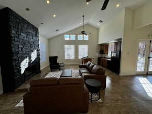 Tiled living room featuring ceiling fan, a stone fireplace, and high vaulted ceiling