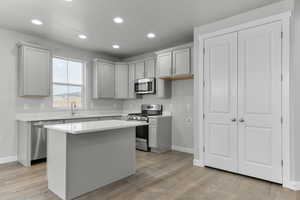 Kitchen with appliances with stainless steel finishes, gray cabinets, a center island, and sink