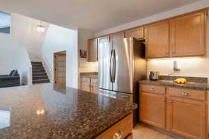 Kitchen with dark stone countertops, hanging light fixtures, stainless steel fridge, and light hardwood / wood-style flooring