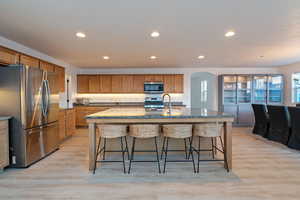 Kitchen with a kitchen island with sink, light hardwood / wood-style floors, a breakfast bar, and appliances with stainless steel finishes