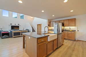 Kitchen with sink, dark stone countertops, an island with sink, stainless steel appliances, and light hardwood / wood-style floors