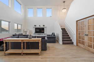 Living room with french doors, a healthy amount of sunlight, a high ceiling, and light wood-type flooring