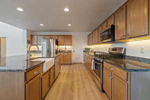 Kitchen with appliances with stainless steel finishes, sink, light wood-type flooring, and dark stone counters