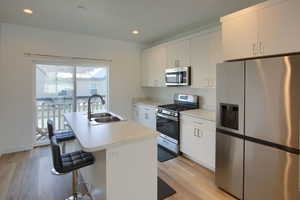 Kitchen with appliances with stainless steel finishes, sink, a center island with sink, and white cabinets