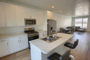 Kitchen featuring appliances with stainless steel finishes, a kitchen island with sink, sink, and white cabinets