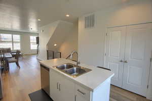 Kitchen featuring sink, light hardwood / wood-style flooring, stainless steel dishwasher, a kitchen island with sink, and white cabinets