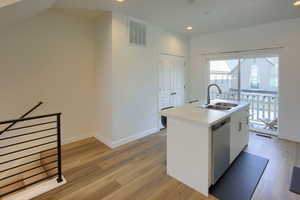 Kitchen featuring sink, light hardwood / wood-style flooring, dishwasher, white cabinets, and a center island with sink