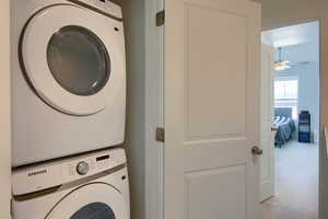 Clothes washing area featuring stacked washer and dryer, light colored carpet, and a textured ceiling