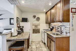 Kitchen featuring a breakfast bar, sink, tasteful backsplash, light stone counters, and white appliances