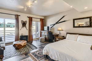 Bedroom with rail lighting, dark hardwood / wood-style floors, and access to exterior