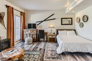 Bedroom featuring multiple windows, dark wood-type flooring, ceiling fan, and a wood stove