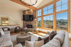 Living room featuring wood finished floors, baseboards, high vaulted ceiling, a fireplace, and a chandelier