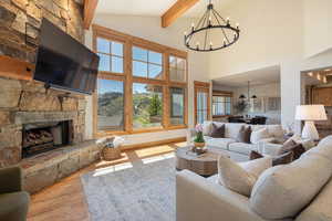 Living room featuring a chandelier, beamed ceiling, wood finished floors, high vaulted ceiling, and a fireplace