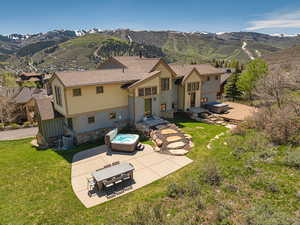 Rear view of property featuring a patio, a mountain view, stone siding, and a lawn