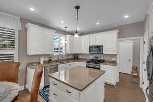 Kitchen featuring sink, white cabinetry, stainless steel appliances, a center island, and decorative light fixtures