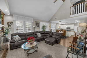 Living room featuring ceiling fan with notable chandelier, high vaulted ceiling, and light wood-type flooring