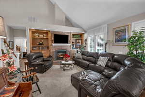 Carpeted living room featuring a brick fireplace, vaulted ceiling, and built in features