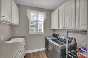 Washroom featuring cabinets, sink, independent washer and dryer, and light hardwood / wood-style flooring