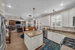 Kitchen featuring sink, white cabinetry, decorative light fixtures, vaulted ceiling, and appliances with stainless steel finishes