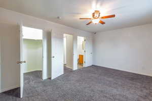 Unfurnished bedroom with dark colored carpet, a walk in closet, ensuite bath, a closet, and ceiling fan