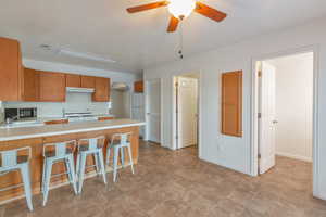 Kitchen with sink, a breakfast bar area, white appliances, kitchen peninsula, and ceiling fan