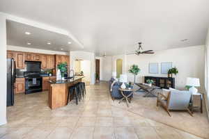 Kitchen featuring light tile patterned floors, a breakfast bar, tasteful backsplash, black appliances, and an island with sink