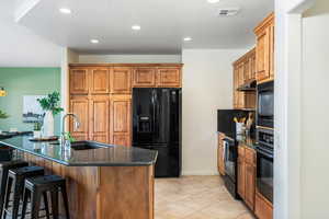 Kitchen featuring sink, light tile patterned floors, a breakfast bar area, black appliances, and dark stone counters