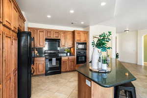 Kitchen featuring tasteful backsplash, dark stone countertops, a kitchen bar, light tile patterned floors, and black appliances