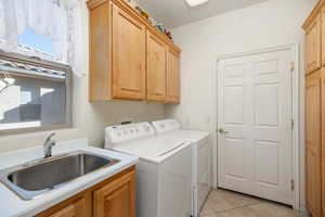 Laundry area featuring cabinets, separate washer and dryer, sink, and light tile patterned floors