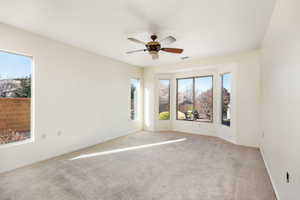 Unfurnished room with ceiling fan, light colored carpet, and a wealth of natural light