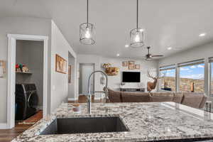 Kitchen with decorative light fixtures, washer / dryer, sink, light stone countertops, and a textured ceiling