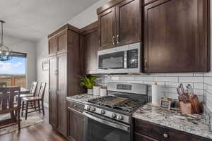 Kitchen with light stone counters, appliances with stainless steel finishes, dark hardwood / wood-style flooring, pendant lighting, and backsplash