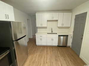 Kitchen with white cabinetry, sink, light hardwood / wood-style flooring, and appliances with stainless steel finishes