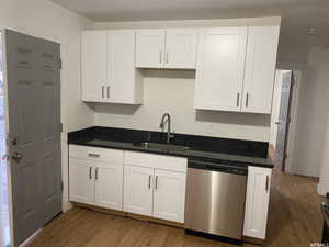 Kitchen with sink, white cabinetry, dark stone countertops, dishwasher, and light hardwood / wood-style floors