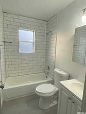 Full bathroom featuring tile patterned flooring, vanity, a textured ceiling, toilet, and tiled shower / bath