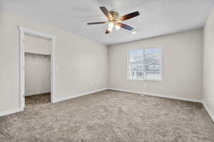 Unfurnished bedroom with a closet, a spacious closet, ceiling fan, and carpet flooring