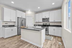 Kitchen featuring sink, appliances with stainless steel finishes, light hardwood / wood-style floors, white cabinets, and a center island with sink