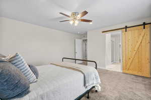 Carpeted bedroom with a barn door and ceiling fan