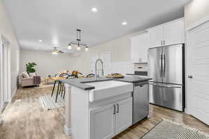 Kitchen with appliances with stainless steel finishes, decorative light fixtures, an island with sink, sink, and white cabinets