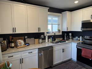 Kitchen featuring light stone countertops, sink, white cabinets, and stainless steel appliances