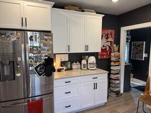 Kitchen with stainless steel fridge with ice dispenser, light wood-type flooring, light stone counters, and white cabinets