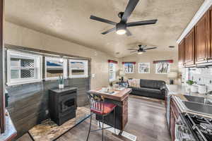 Kitchen featuring vaulted ceiling, dark hardwood / wood-style floors, a wood stove, stainless steel gas range, and a textured ceiling