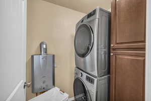 Washroom with stacked washer and dryer, a textured ceiling, cabinets, and water heater