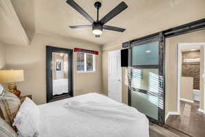 Bedroom with wood-type flooring, a barn door, a textured ceiling, and ceiling fan