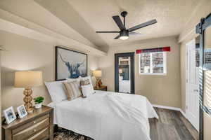 Bedroom featuring lofted ceiling, dark wood-type flooring, ceiling fan, a textured ceiling, and a barn door