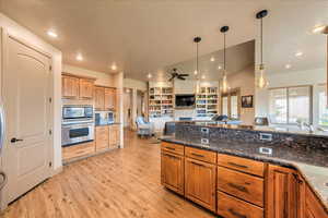 Kitchen featuring light hardwood / wood-style floors, decorative light fixtures, stainless steel appliances, and dark stone counters