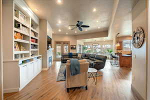 Living room with built in features, light hardwood / wood-style floors, and ceiling fan