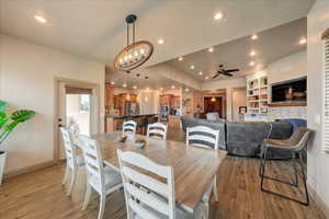 Dining space with ceiling fan with notable chandelier, a fireplace, built in shelves, and light wood-type flooring