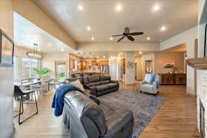 Living room featuring a stone fireplace, ceiling fan with notable chandelier, and light wood-type flooring